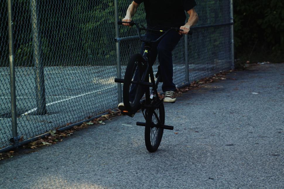Free Image of Man Riding Bike Down Street Next to Fence 