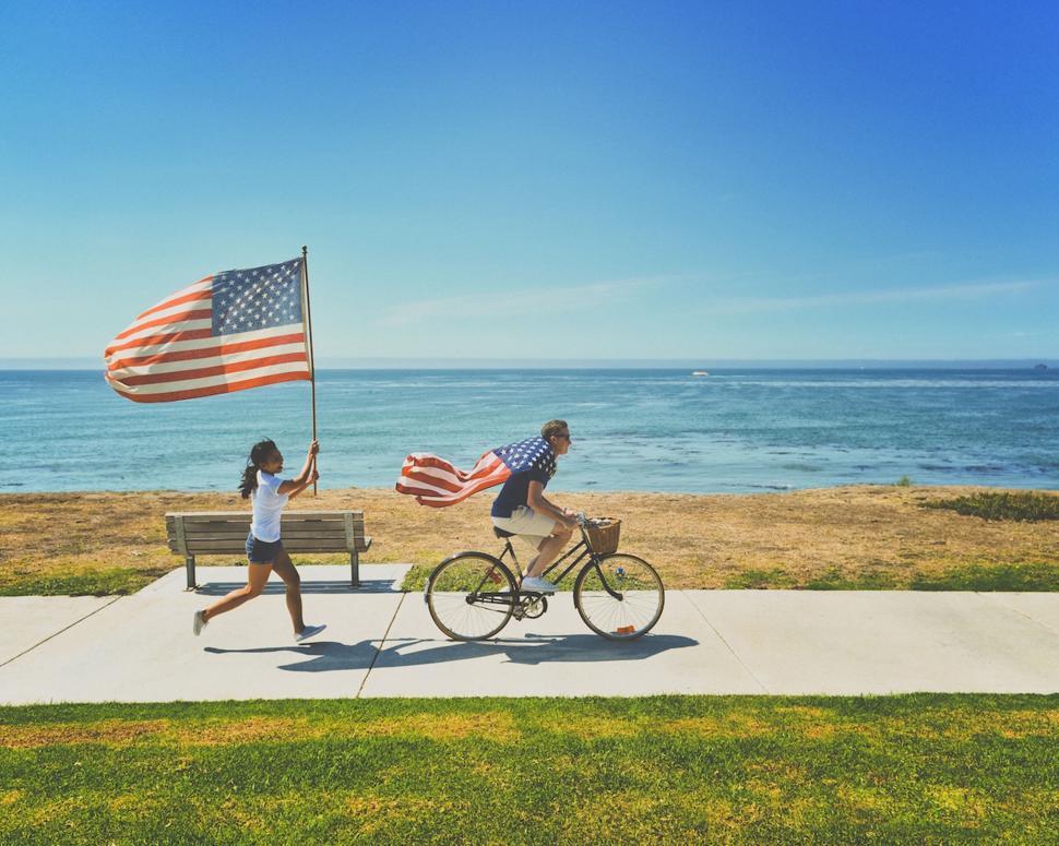 Free Image of Man Riding Bike Next to Woman Holding American Flag 