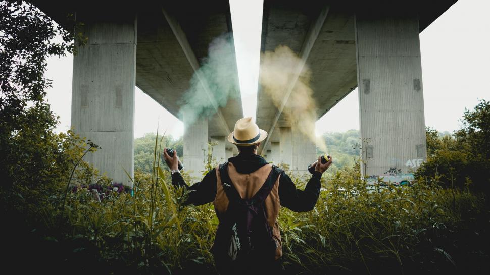 Free Image of Man Standing in Front of Bridge With Smoke Coming Out of His Hands 