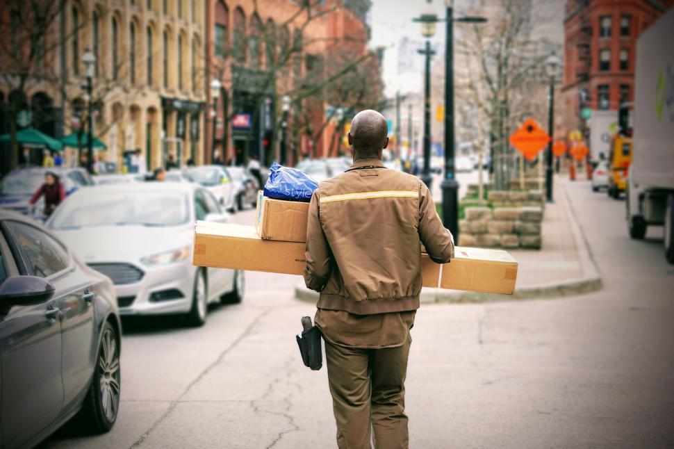 Free Image of Man Walking Down Street Carrying Boxes on His Back 