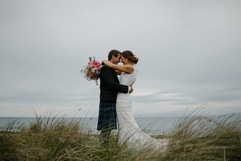 Free Image of Bride and Groom Standing in Tall Grass by the Ocean 
