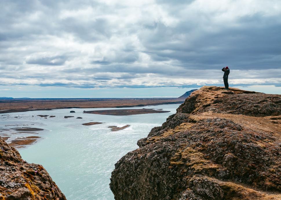 Free Image of Man Standing on Top of Large Rock by Water 