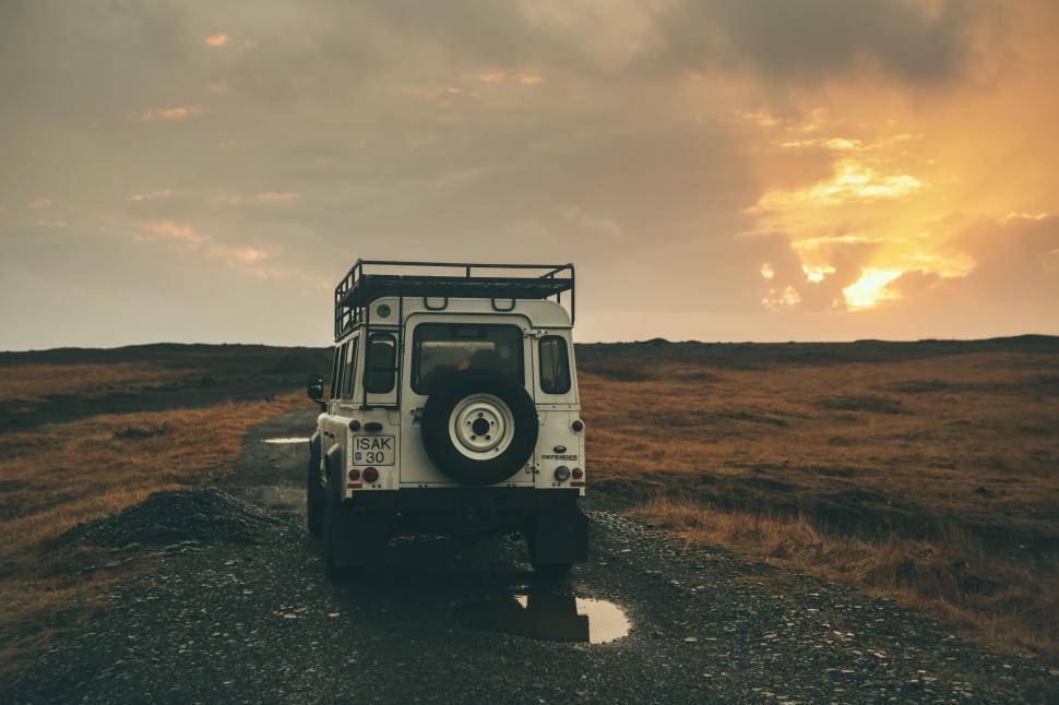 Free Image of Jeep Driving Down Dirt Road Under Cloudy Sky 