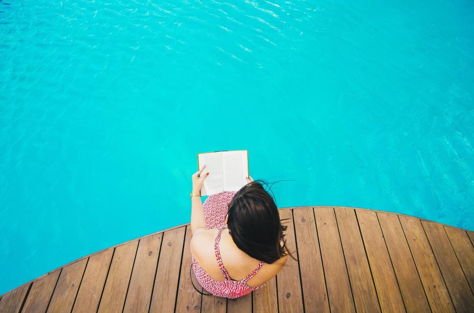 Free Image of Woman Sitting on Wooden Deck Next to Swimming Pool 