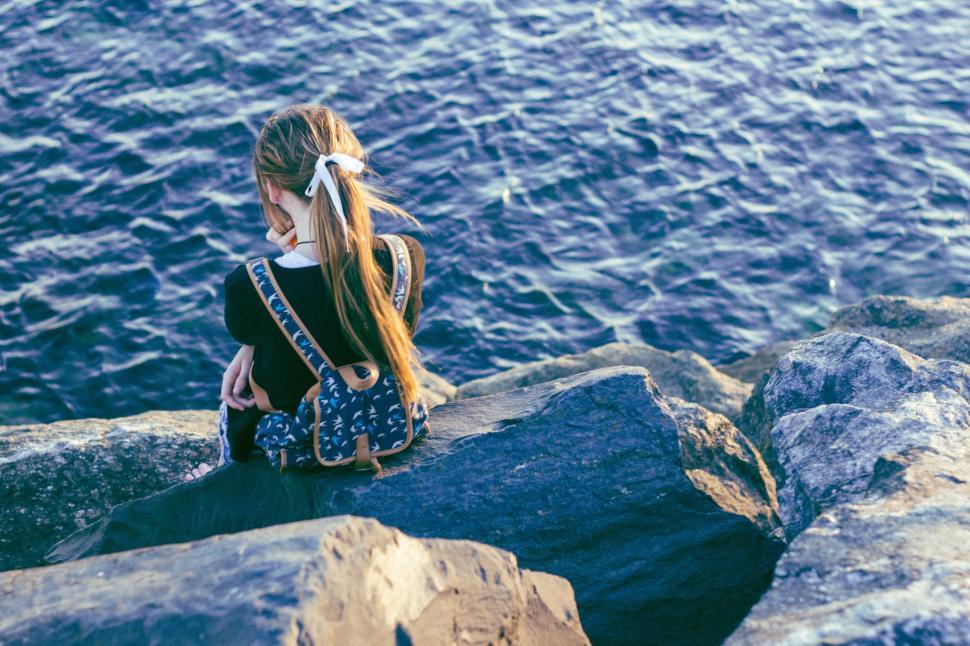 Free Image of Woman Sitting on Rock Next to Body of Water 
