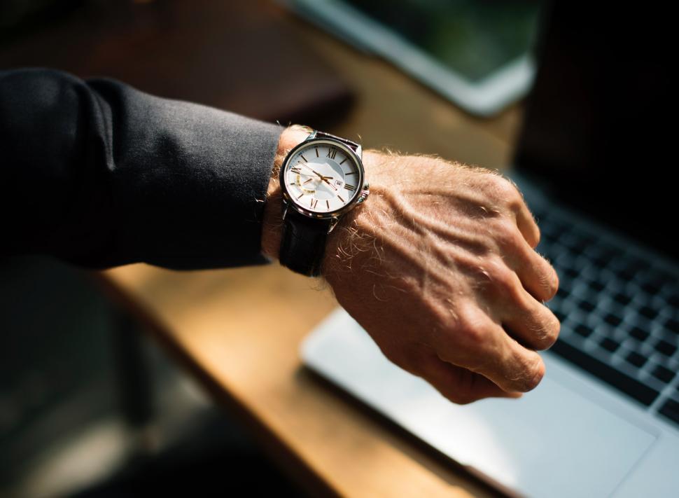 Free Image of Man Holding Watch While Sitting in Front of Laptop 