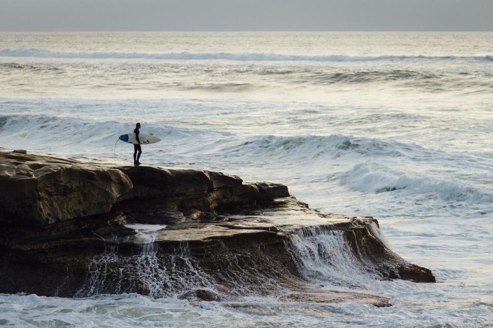 Free Image of Person Holding Surfboard Standing on Rock Near Ocean 