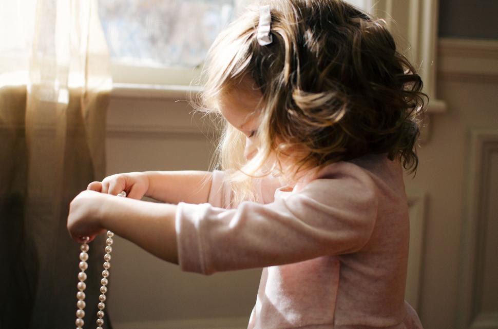 Free Image of Little Girl in Pink Dress Holding Pearl Necklace 