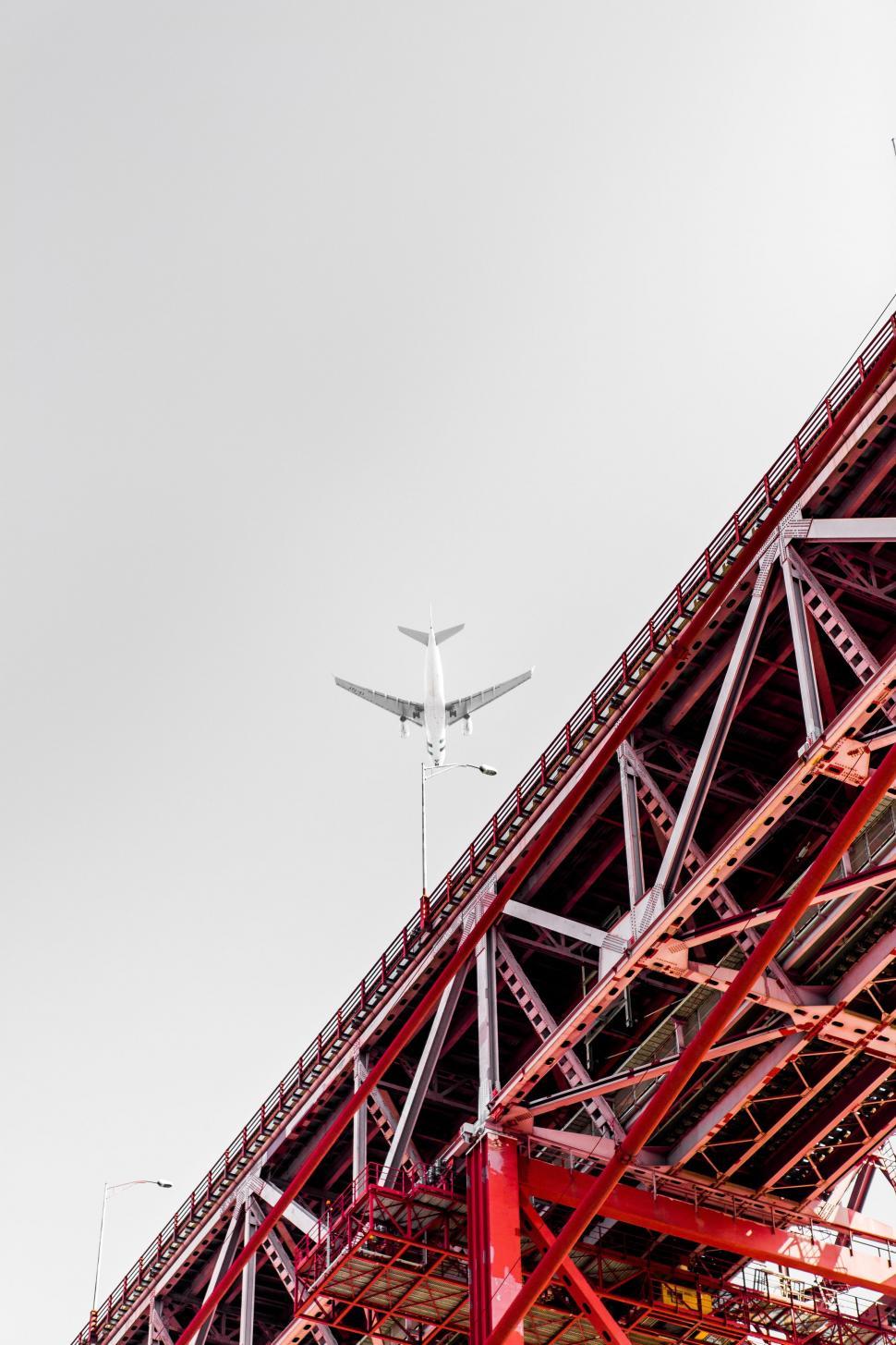 Free Image of Airplane Flying Over Red Bridge 
