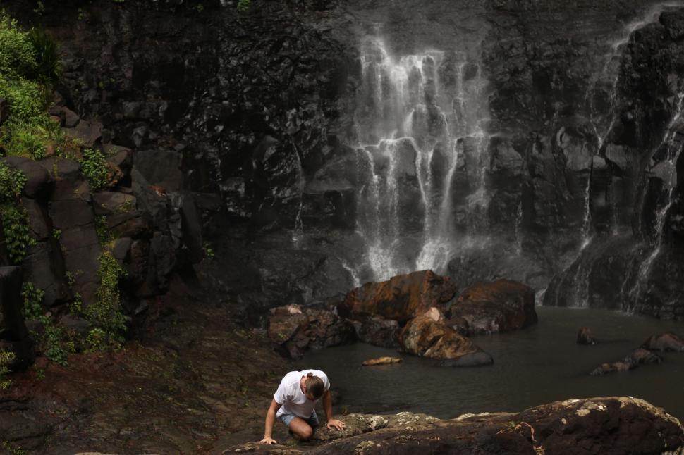 Free Image of Man Kneeling in Front of Waterfall 