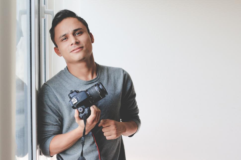 Free Image of Man Holding Camera in Front of Window 