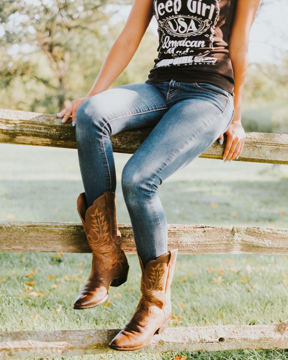 Free Image of Woman Sitting on Fence in Cowboy Boots 
