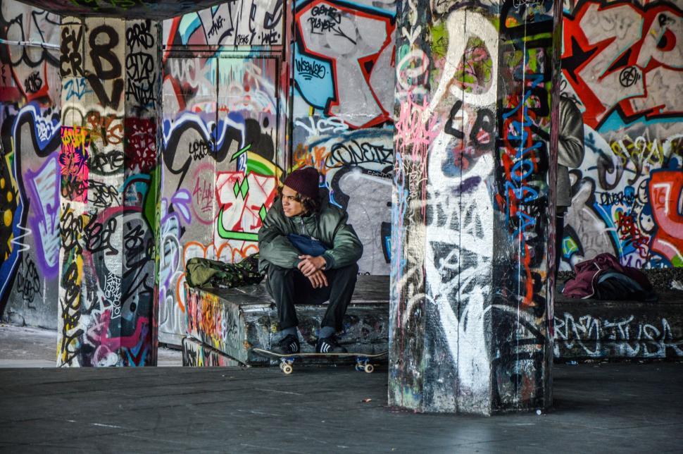 Free Image of Man Sitting on Skateboard in Front of Graffiti Covered Walls 