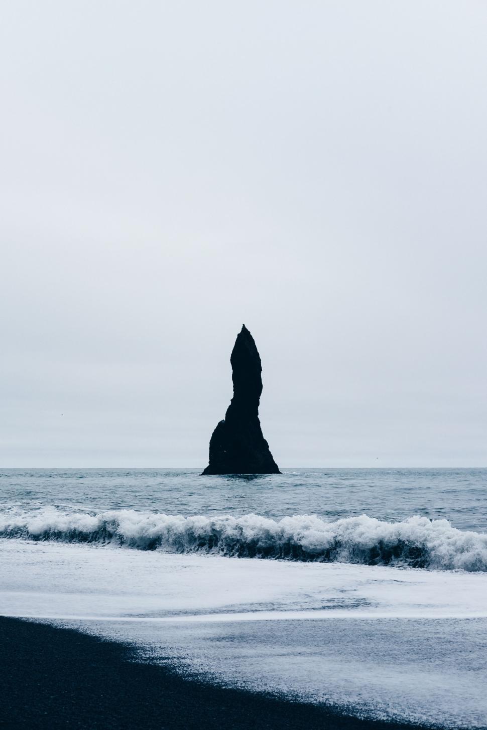 Free Image of Rock Formation Jutting Out of Ocean Next to Beach 