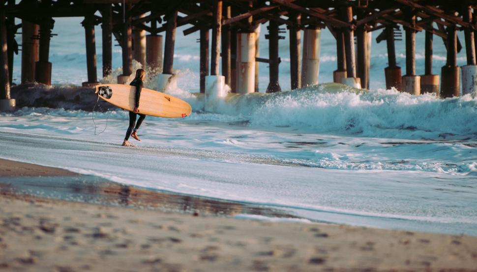 Free Image of Person Carrying Surfboard Under Pier 