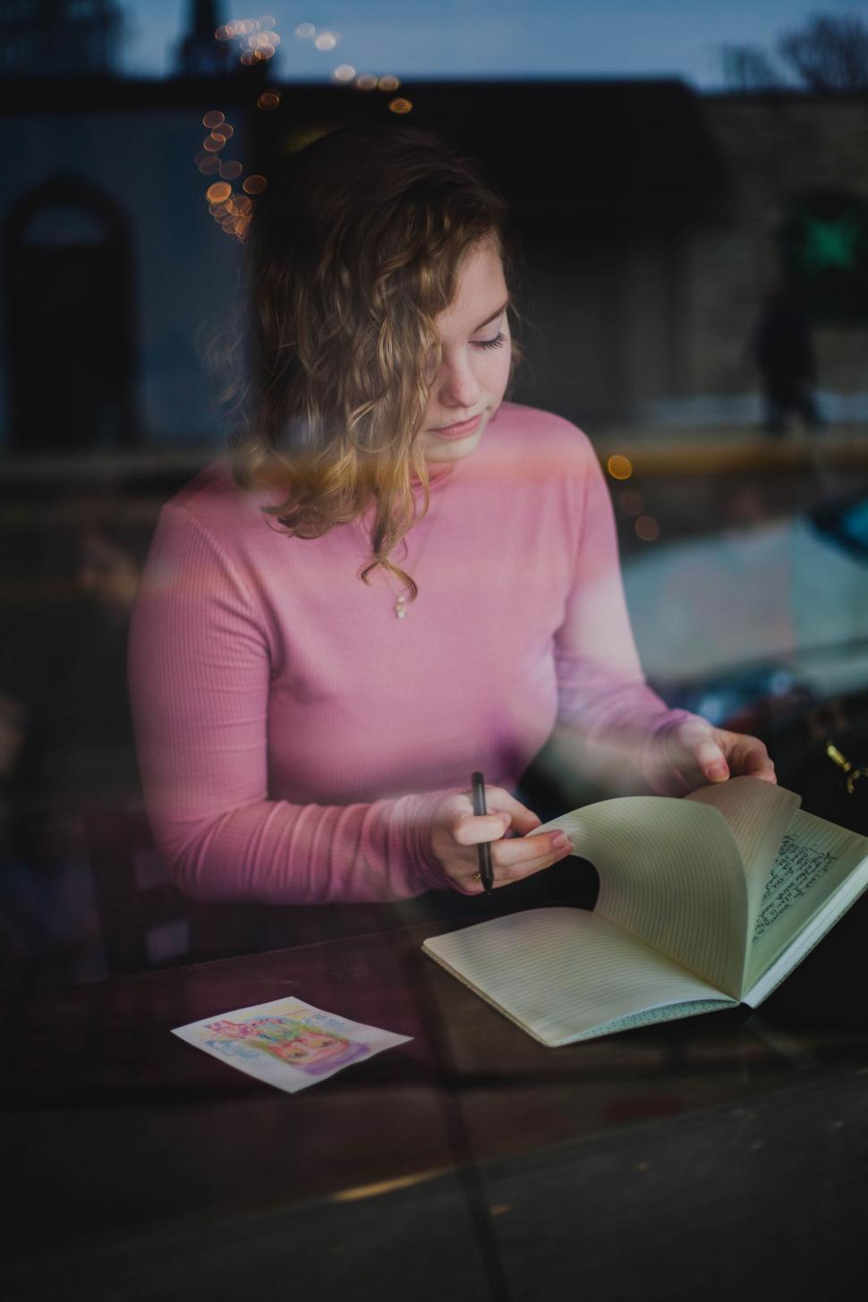 Free Image of Woman Sitting at Table With Book and Pen 