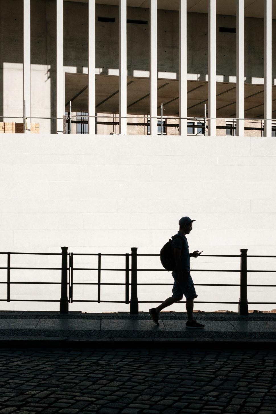 Free Image of Man Walking Down Sidewalk Next to Tall Building 