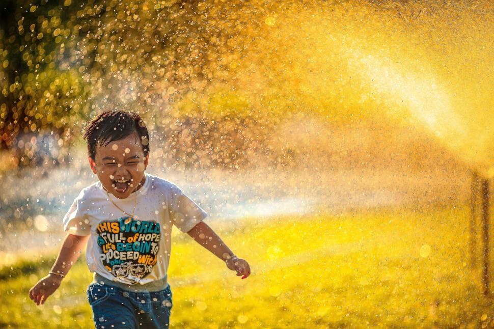 Free Image of Young Boy Running Through a Sprinkle of Water 