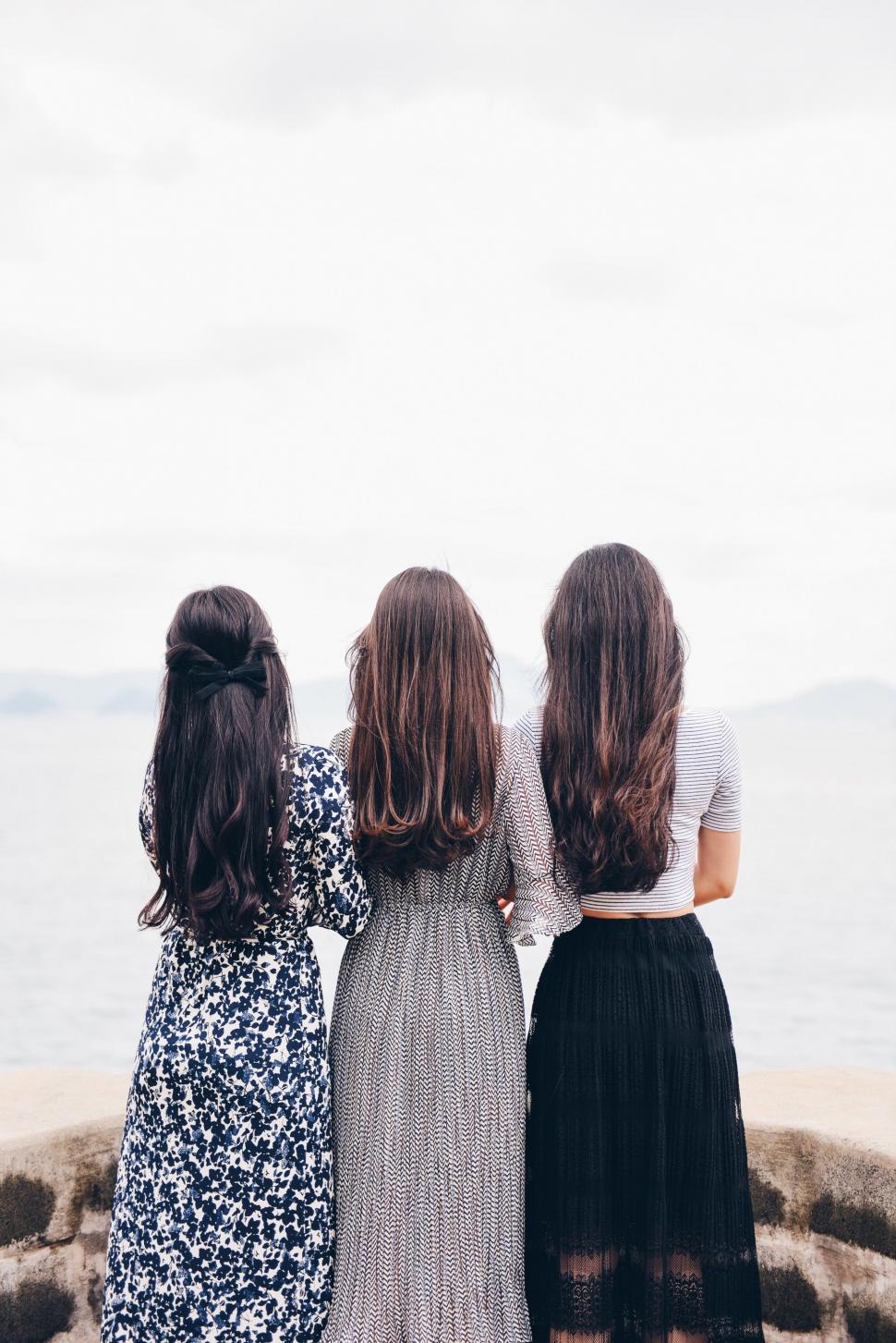 Free Image of Three Women Standing on a Beach Looking at the Water 