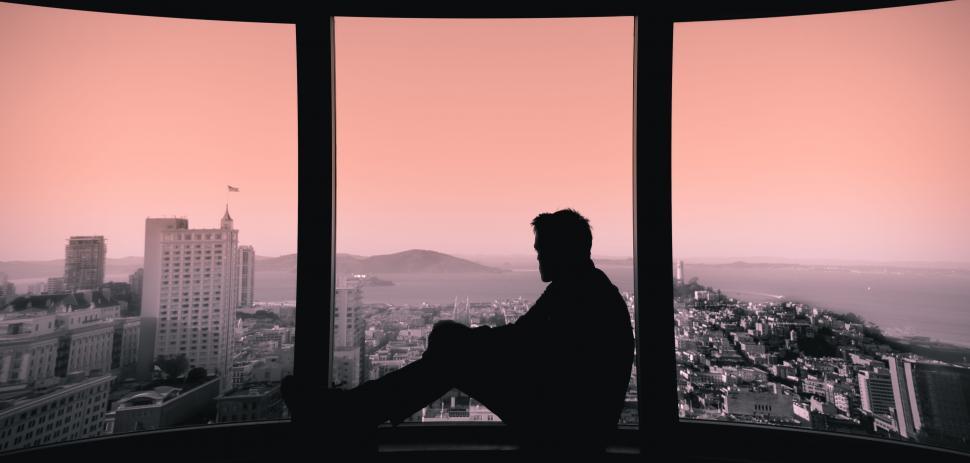 Free Image of Man Sitting on Window Sill Looking Out at City 