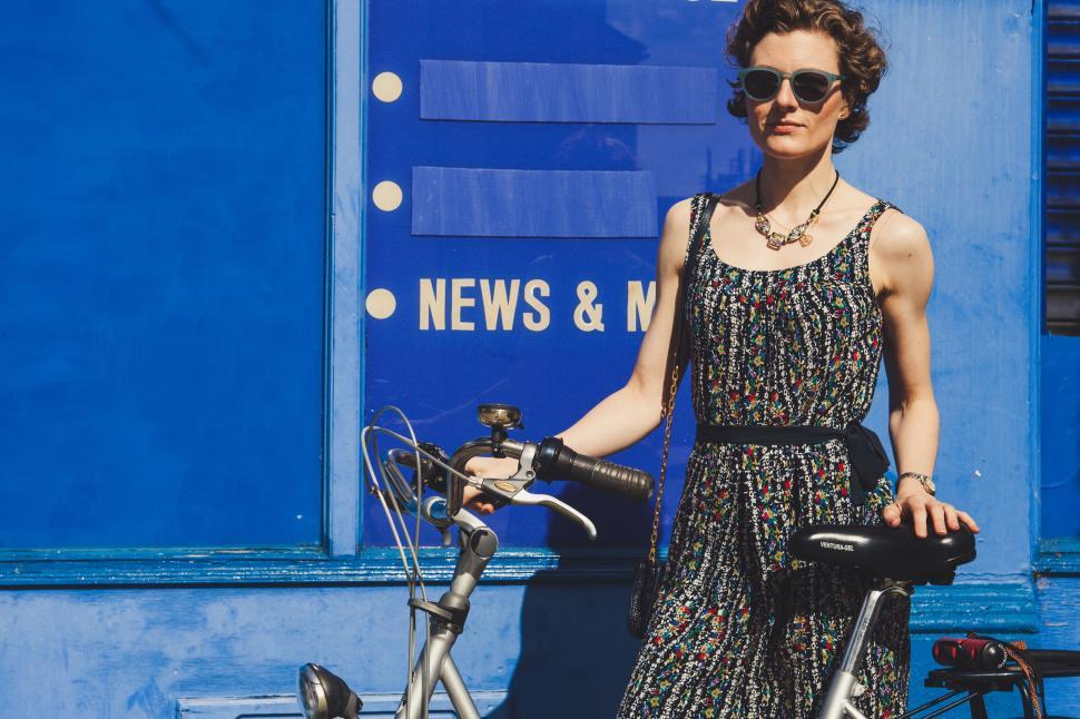 Free Image of Woman Standing Next to a Bike in Front of a Blue Building 