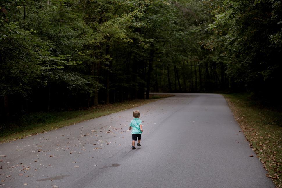 Free Image of Little Boy Walking Down a Road in the Middle of a Forest 