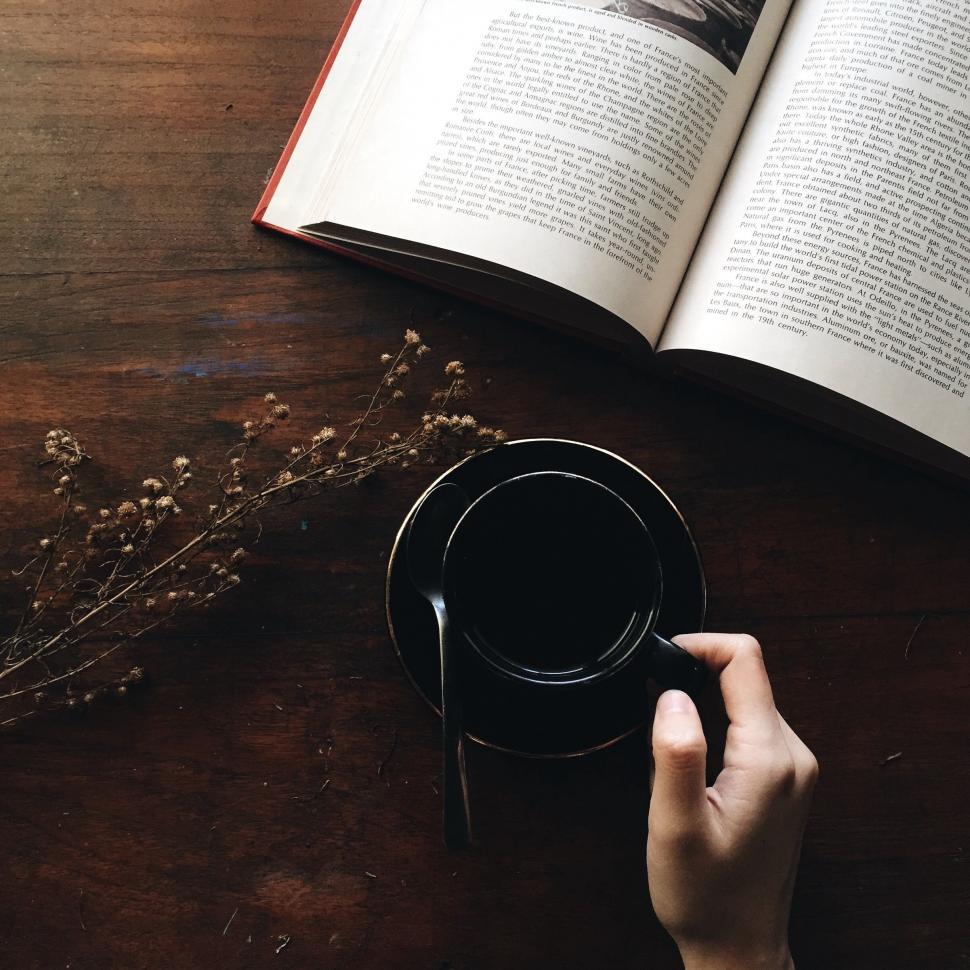 Free Image of Person Holding Coffee Cup in Front of Open Book 